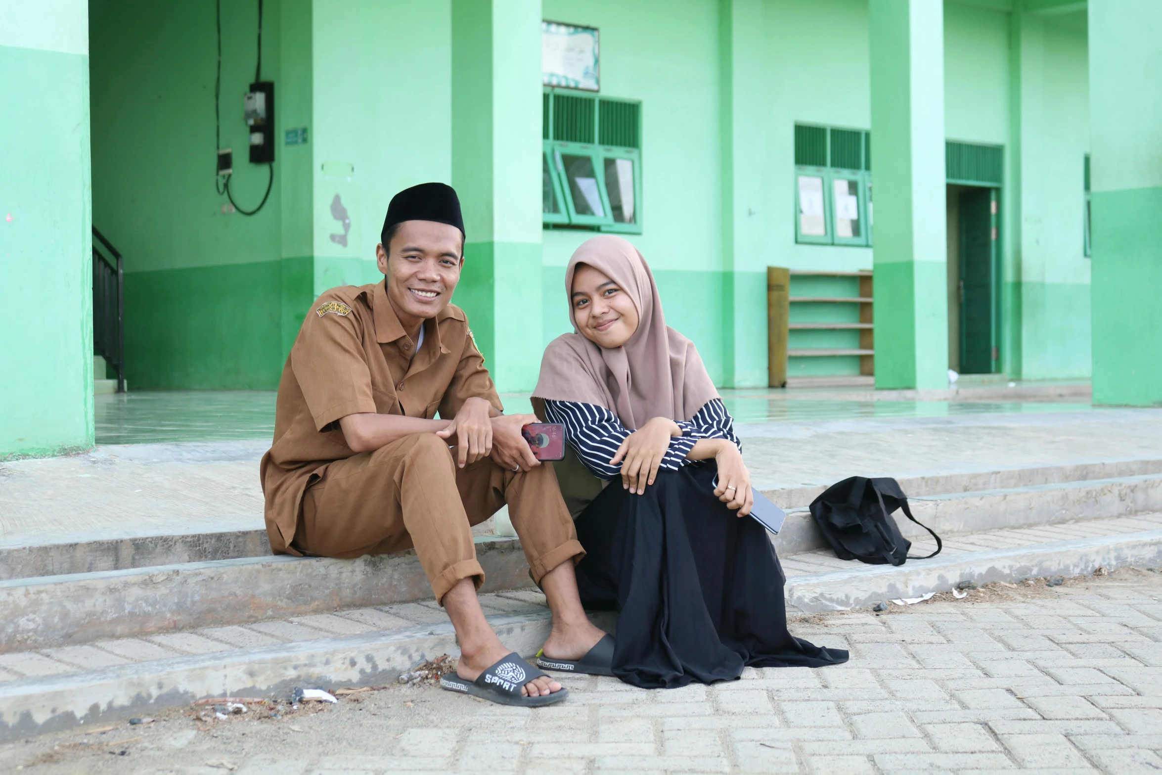 a couple in hijab sit on the stairs of a building