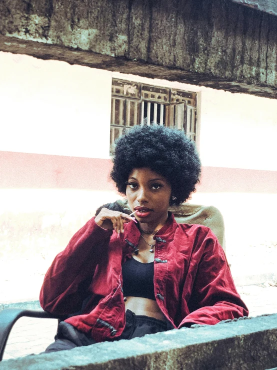 a woman is leaning against a wall with a red jacket on