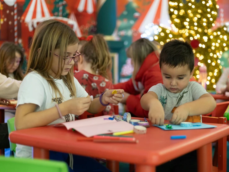 there are children sitting at a red table doing crafts