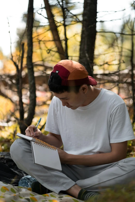 a boy sitting in the woods writing on a notebook