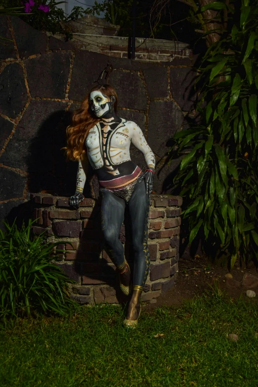 a man wearing makeup and skeleton costume next to a stone wall