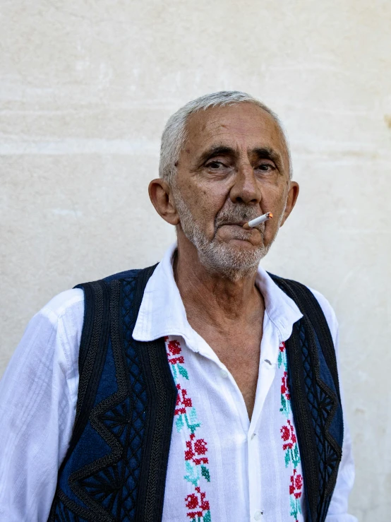 a man wearing an vest, white shirt and blue flowered shirt smoking a cigarette