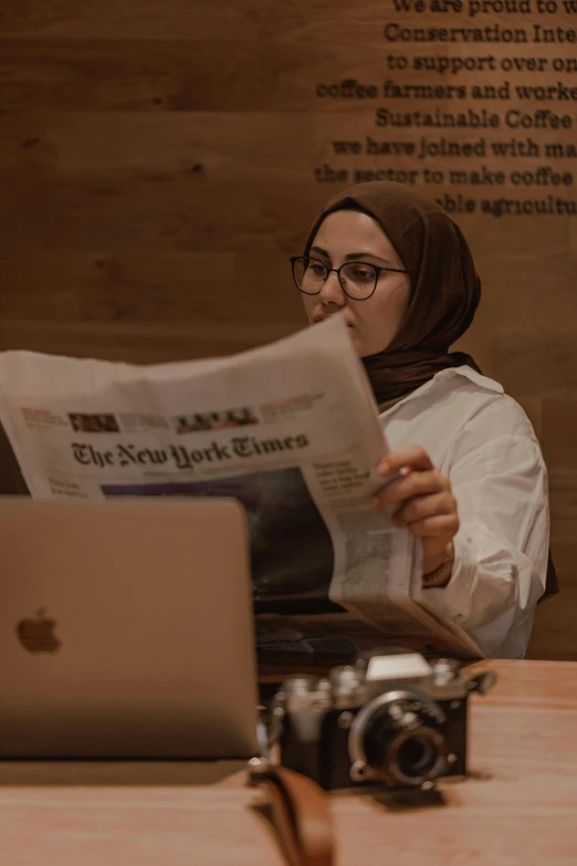 a woman in hijab reading the paper on her laptop