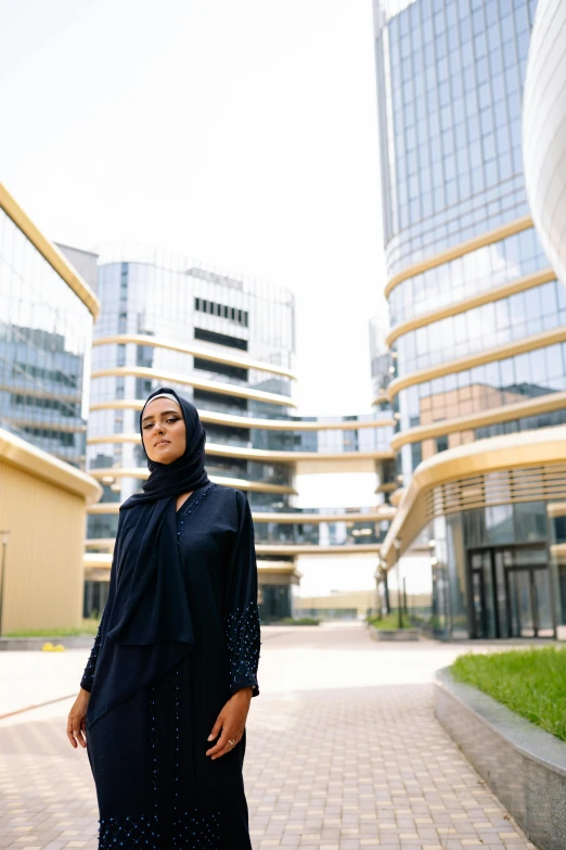 a woman stands outside in a black dress and head scarf