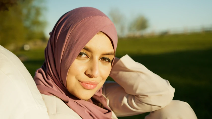 a woman sitting outside wearing a pink headscarf