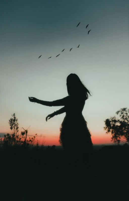 a woman standing in front of a sunset holding her hands out to the sun