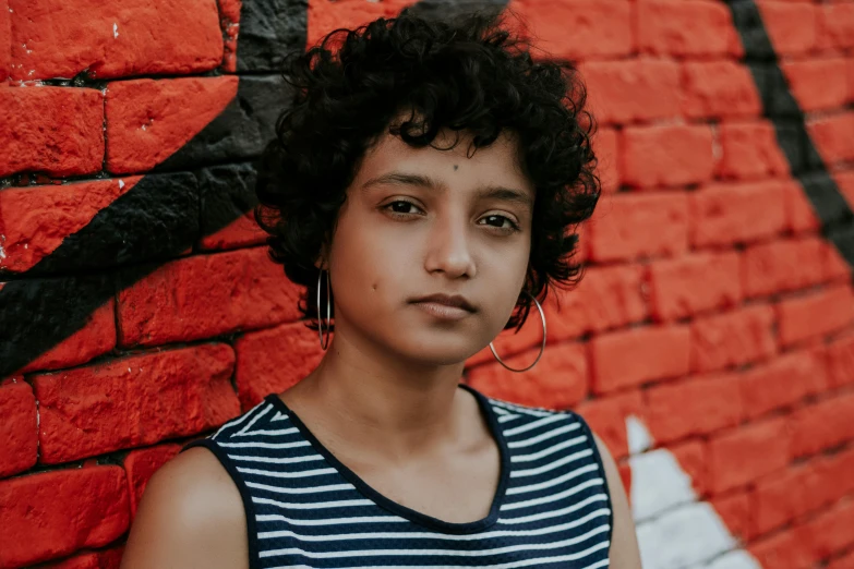 a young woman stands in front of a painted brick wall