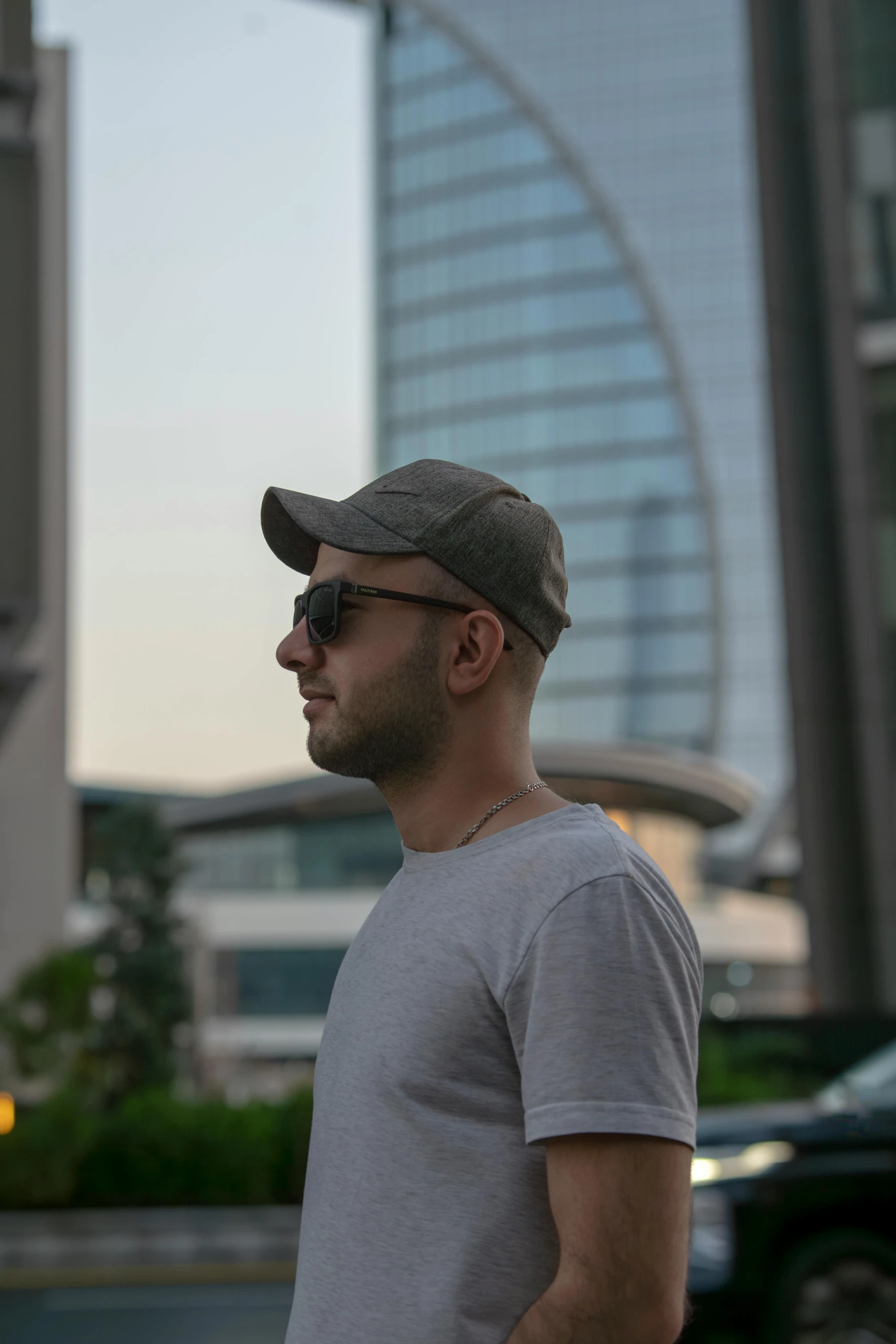 a man wearing shades and a hat stands on a sidewalk