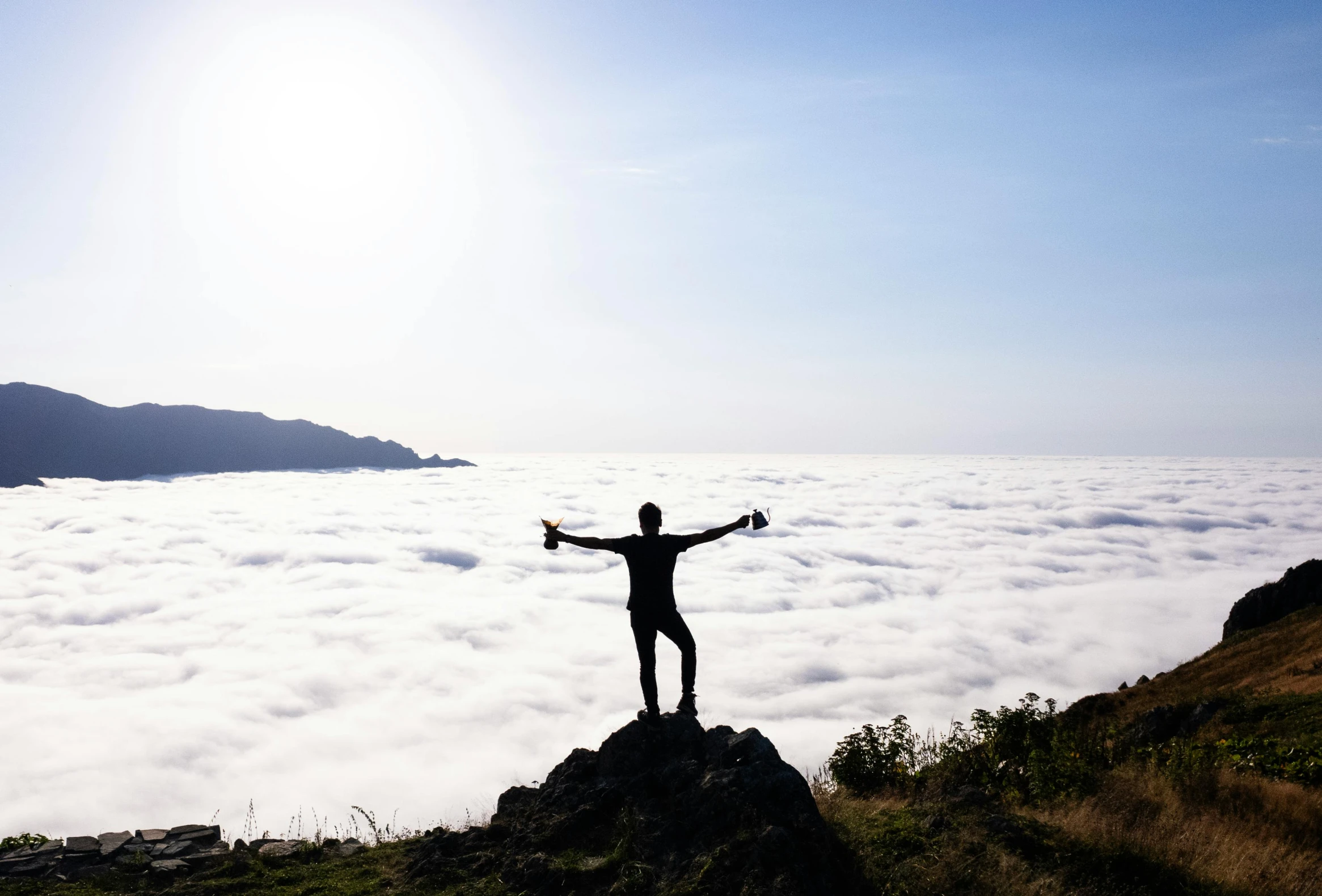man standing on top of the hill with arms raised above clouds