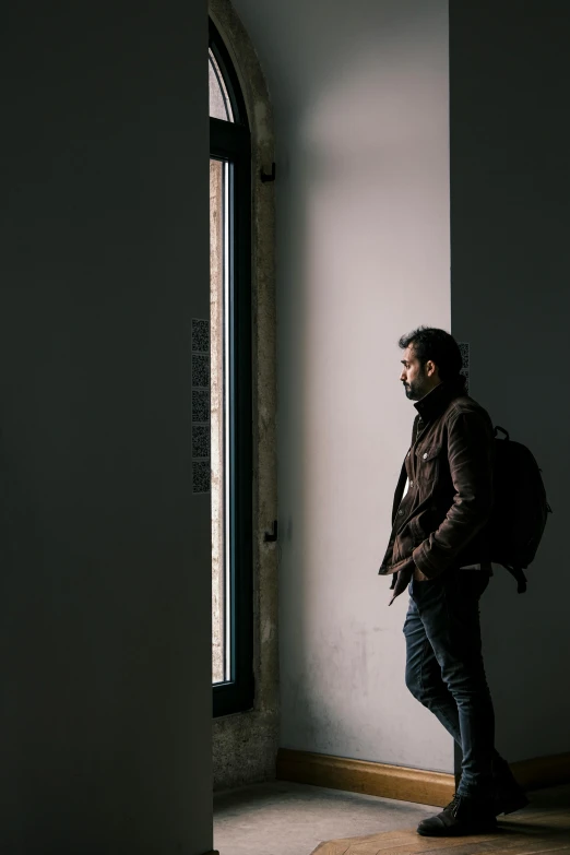 man looking out window standing by white wall