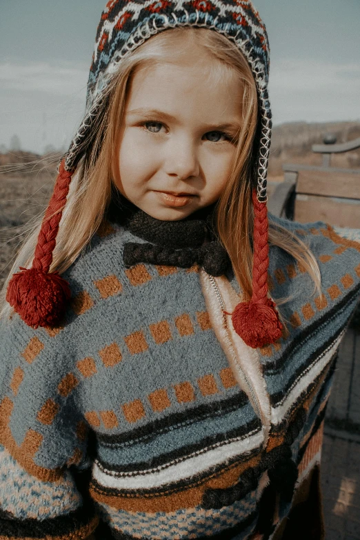 a young blonde girl wearing a sweater and a scarf