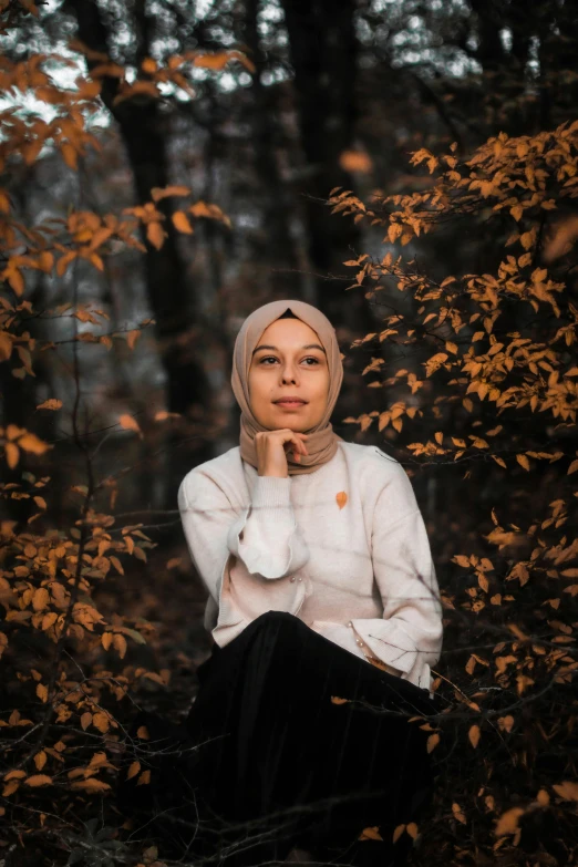 a woman wearing a hijab sitting in the woods