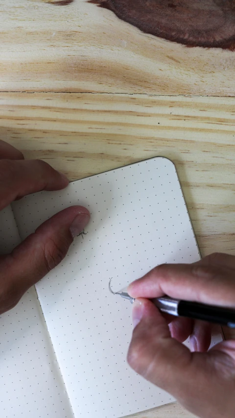 a person holding a pen is writing on a notepad