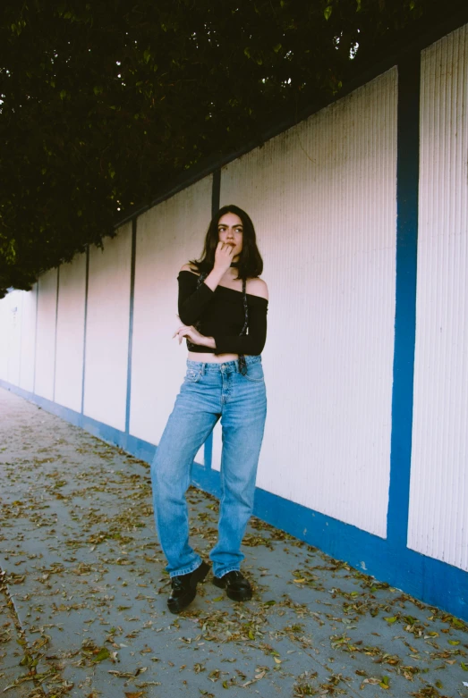 woman wearing jeans leaning against wall in black shirt