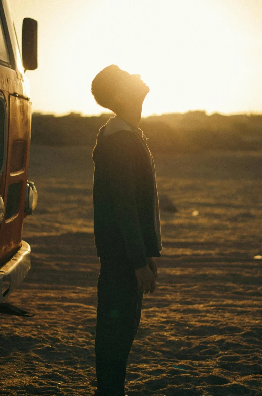 man standing next to van with bright yellow sun behind him