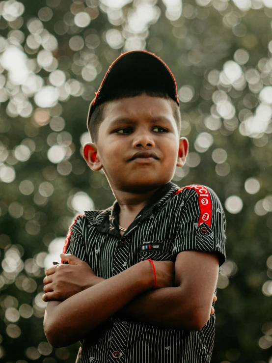 a boy standing in front of trees, wearing a striped shirt