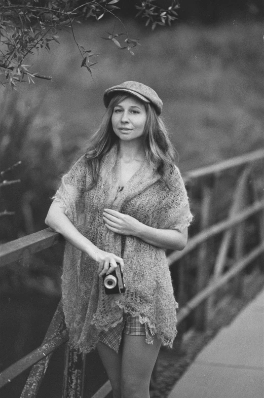 a woman in a hat and sweater standing next to a wooden fence