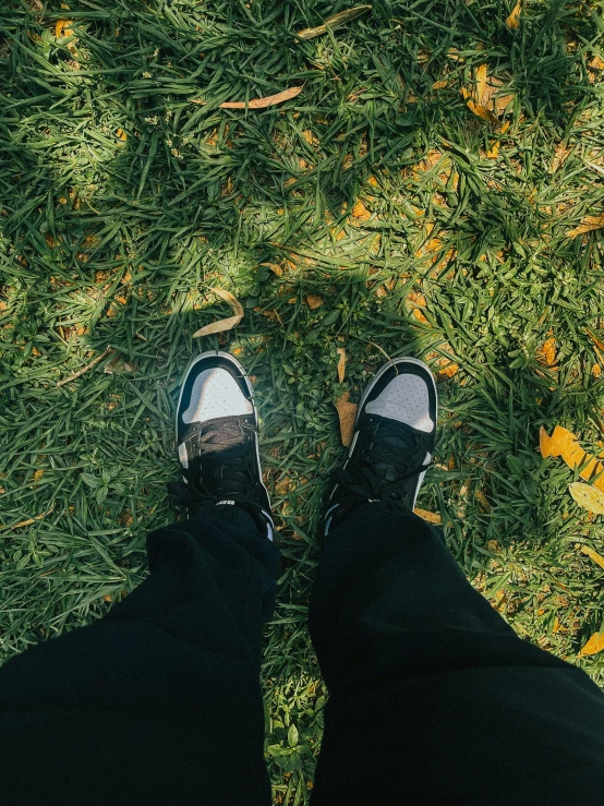 a person's feet in jeans and sneakers looking down at grass with leaves scattered about them