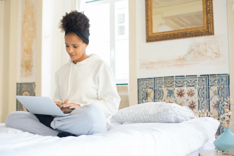 a woman sitting on top of a bed using her laptop