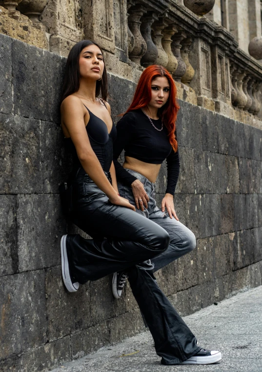 two woman are leaning against a wall next to each other