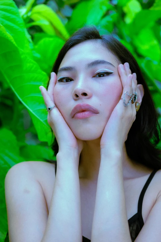 a woman standing in front of leaves with her hands on her face