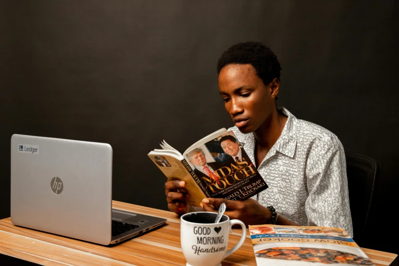 a man is reading the book while using a computer