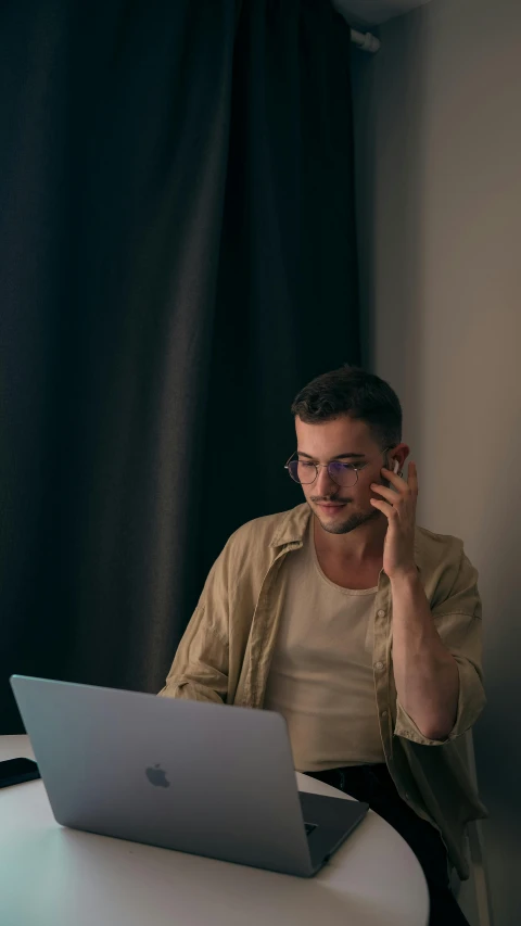 man sitting at table using laptop while talking on cellphone