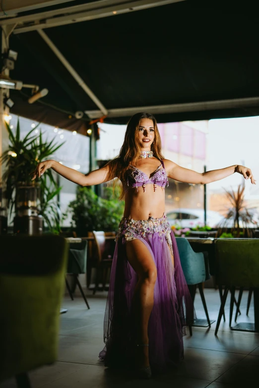 an attractive woman in a purple outfit dancing in front of tables