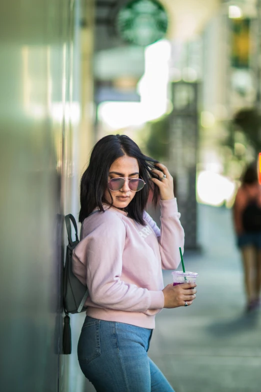 a woman leaning on the wall drinking from a cup