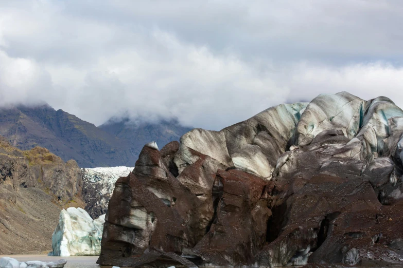 a rock formation by the water with mountains in the background