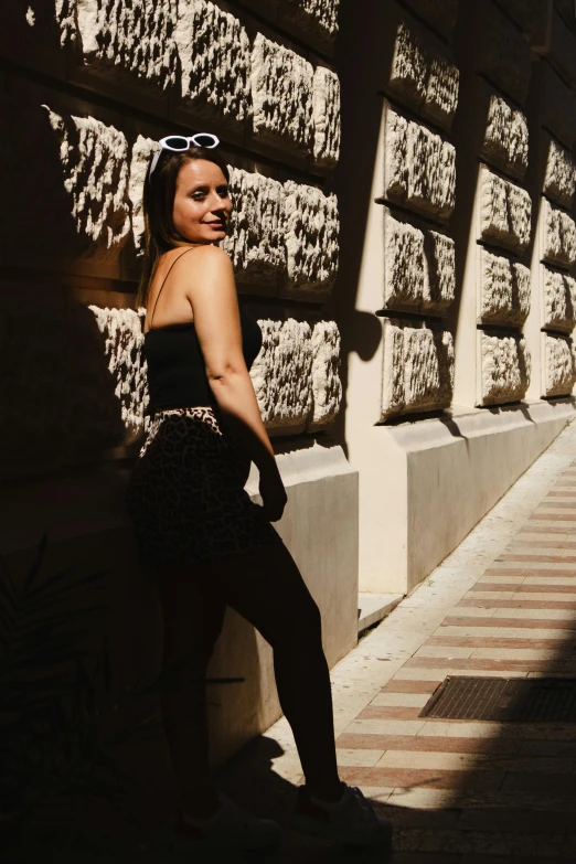 a young lady stands on a curb by a brick wall