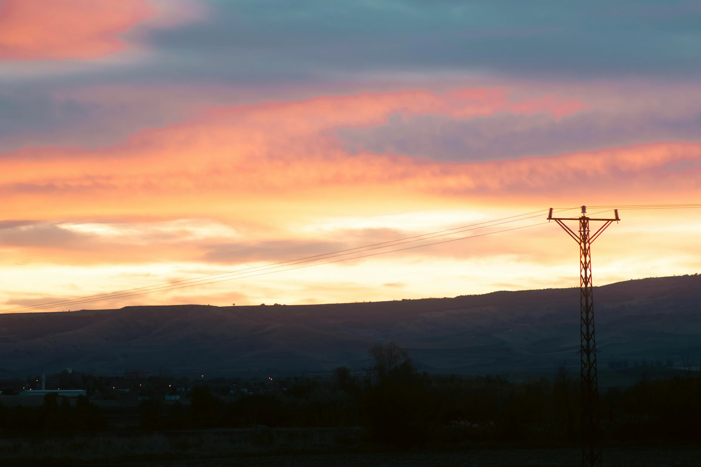 an empty field beneath a mountain with power lines in the foreground