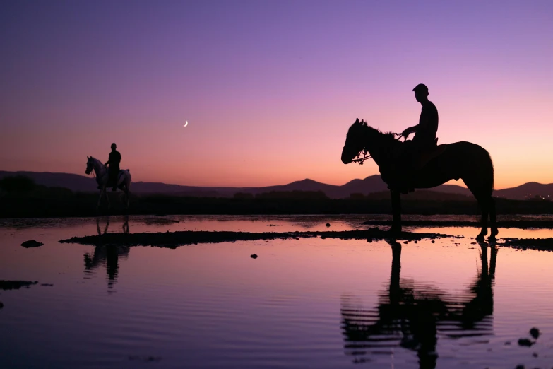 some people riding horses next to the water at dusk