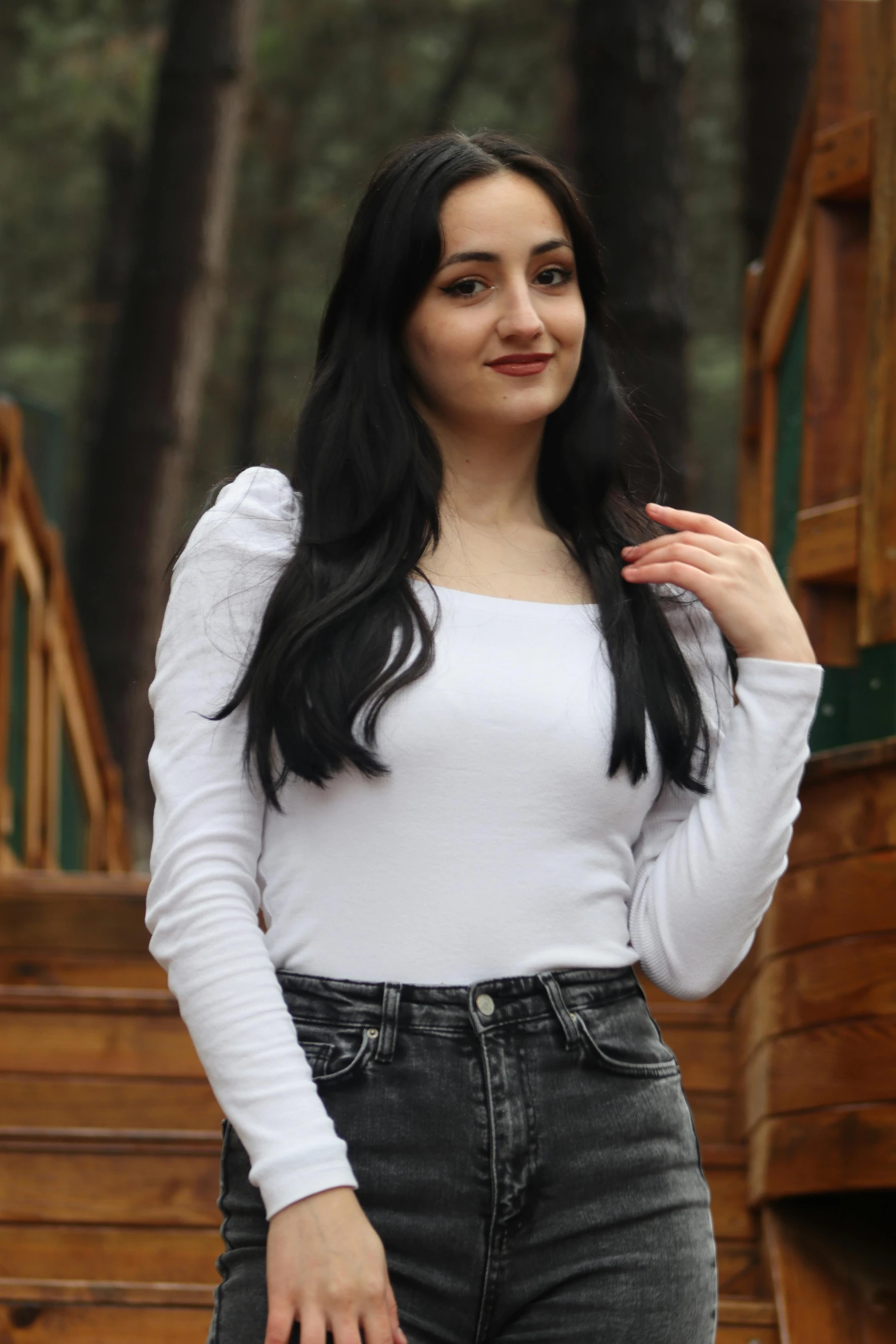 woman with long dark hair wearing jeans and white shirt standing in front of trees