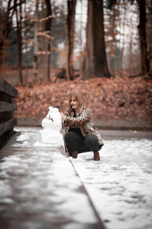 a woman kneeling on the ground in front of a snowman