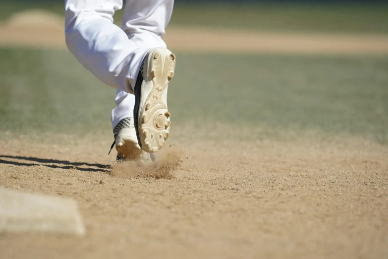 a man in white pants and sneakers kicks up dirt