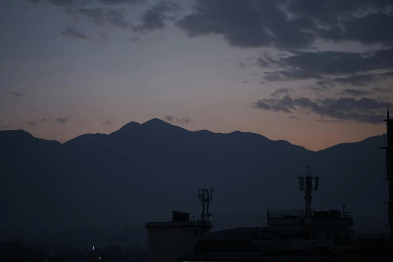 the sky is illuminated by dark clouds as buildings sit in front of the mountains