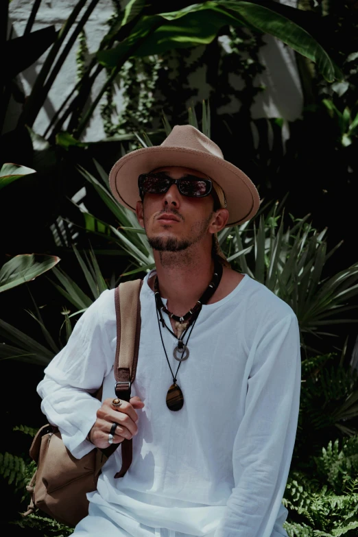 a man wearing sunglasses and a tan hat with a bag