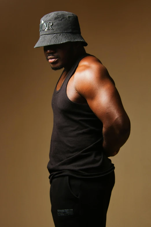 man in black tank and hat standing with his hands on his hips