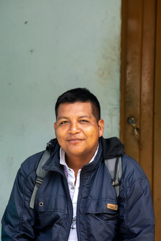 a man sitting down smiling in front of a wall