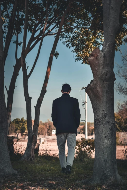 man in black jacket walking through tree lined area