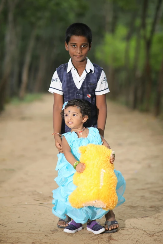 two children on dirt road with trees in the background