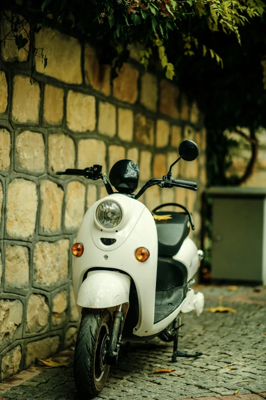 a white scooter parked next to a brick wall