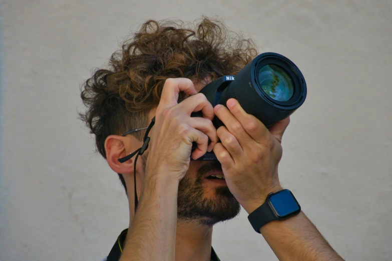 a man with long hair holds up a camera in front of his face