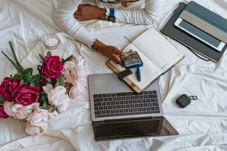 a bed with a laptop and a book with a flower arrangement next to it