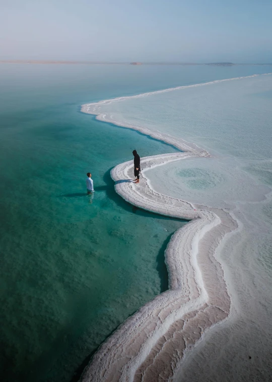 an aerial view shows the water, the shore and the two people walking on the path