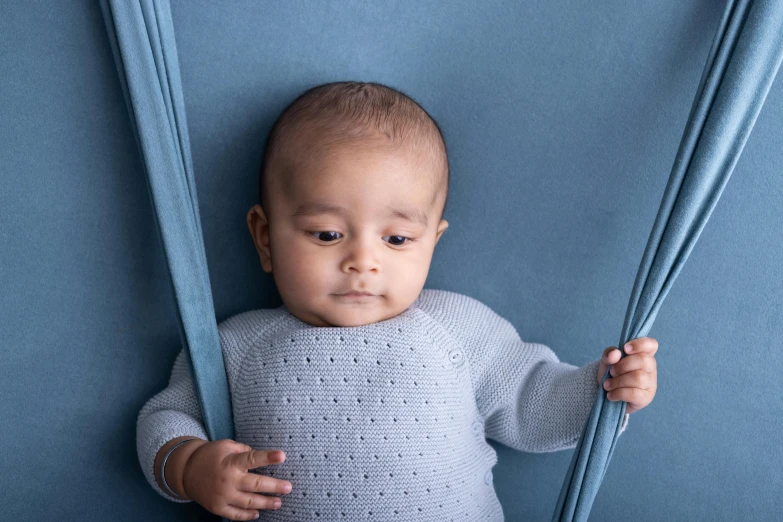 a baby in a blue sweater hiding behind blue sticks