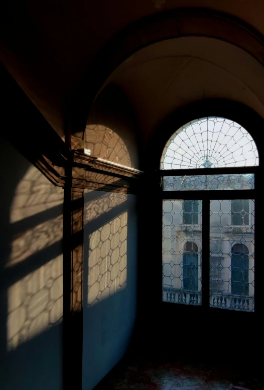 sunlight streams in through two arched windows onto a small wall