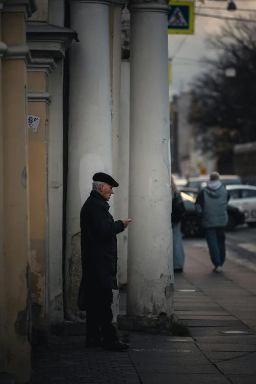 the man stands by the pillars and looks at his phone