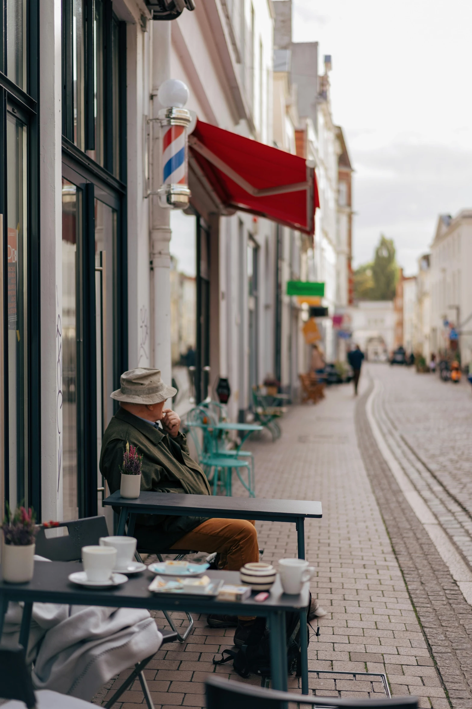 an old man with a hat sits outside a coffee shop